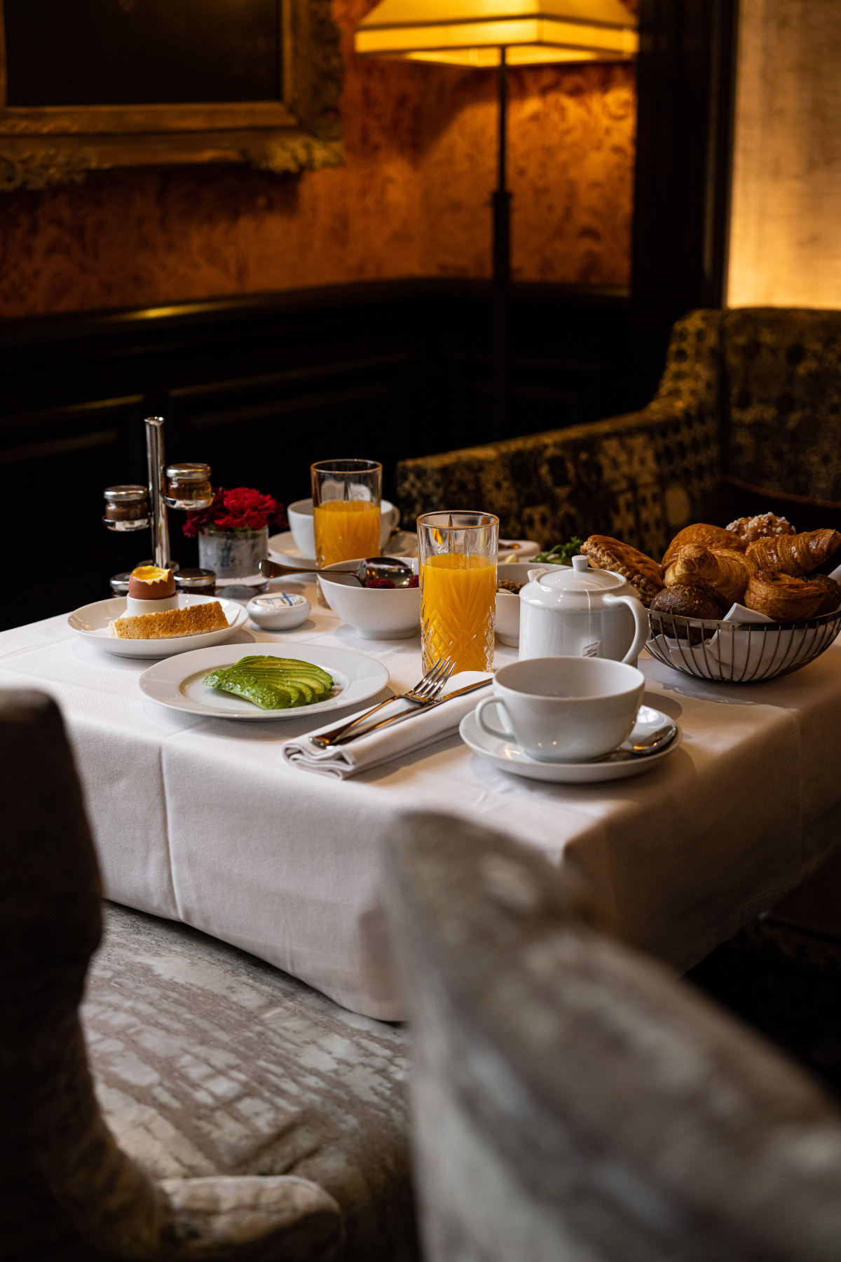 A breakfast table with white linens, pastries, avocado, a soft-boiled egg, and orange juice in a dark-paneled salon at the Pavillon de la Reine.
