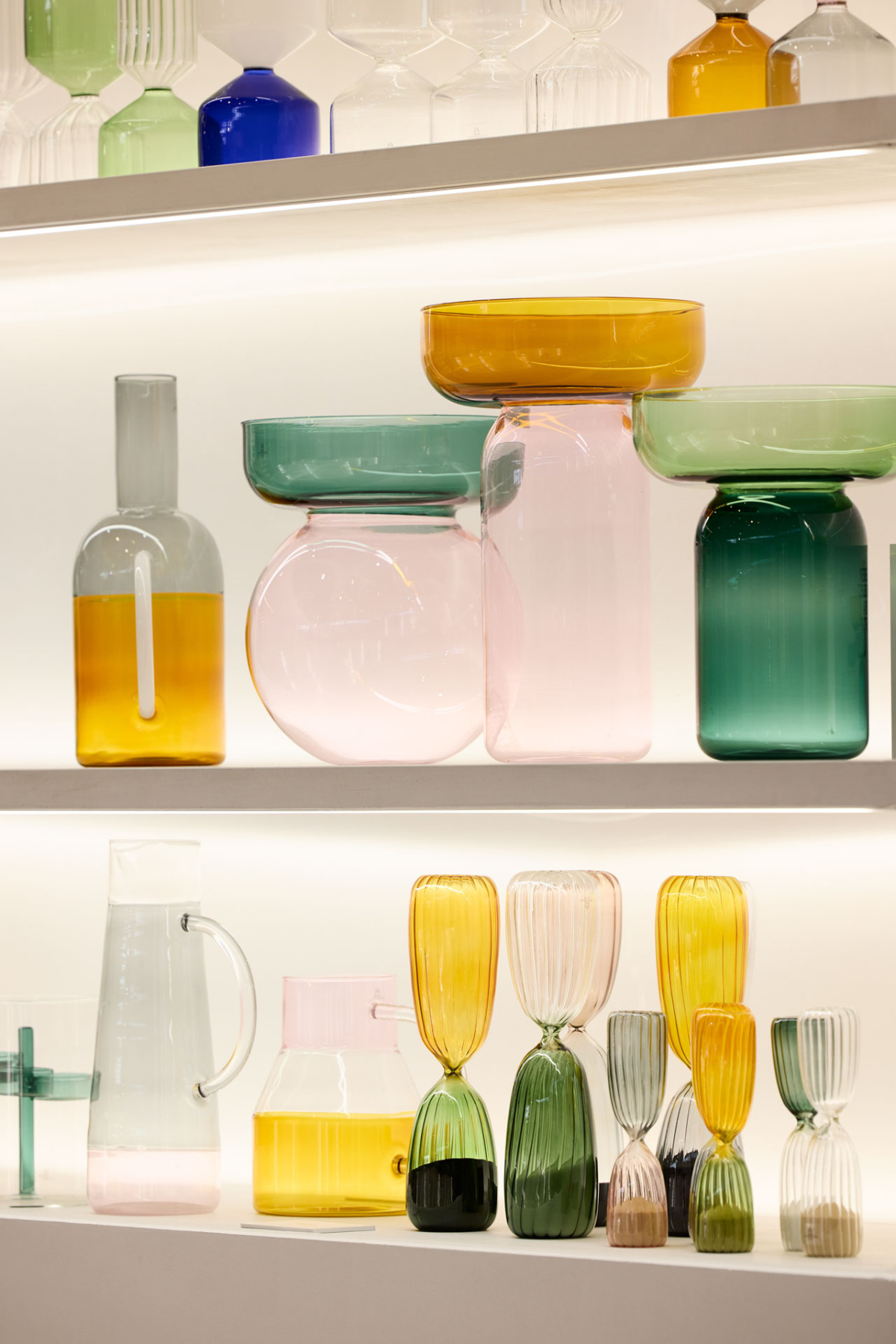 Pastel colored glass vessels on lit white shelves