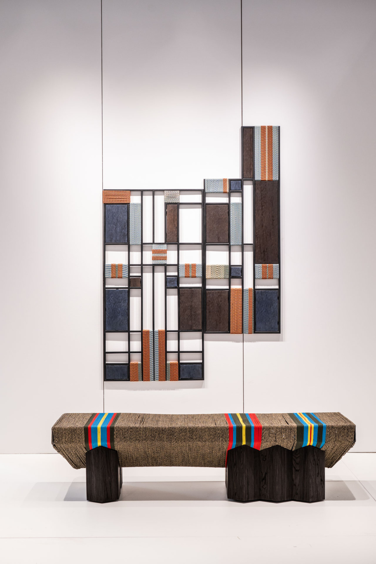 Gridded wooden wall panels above a woven bench with colored stripes