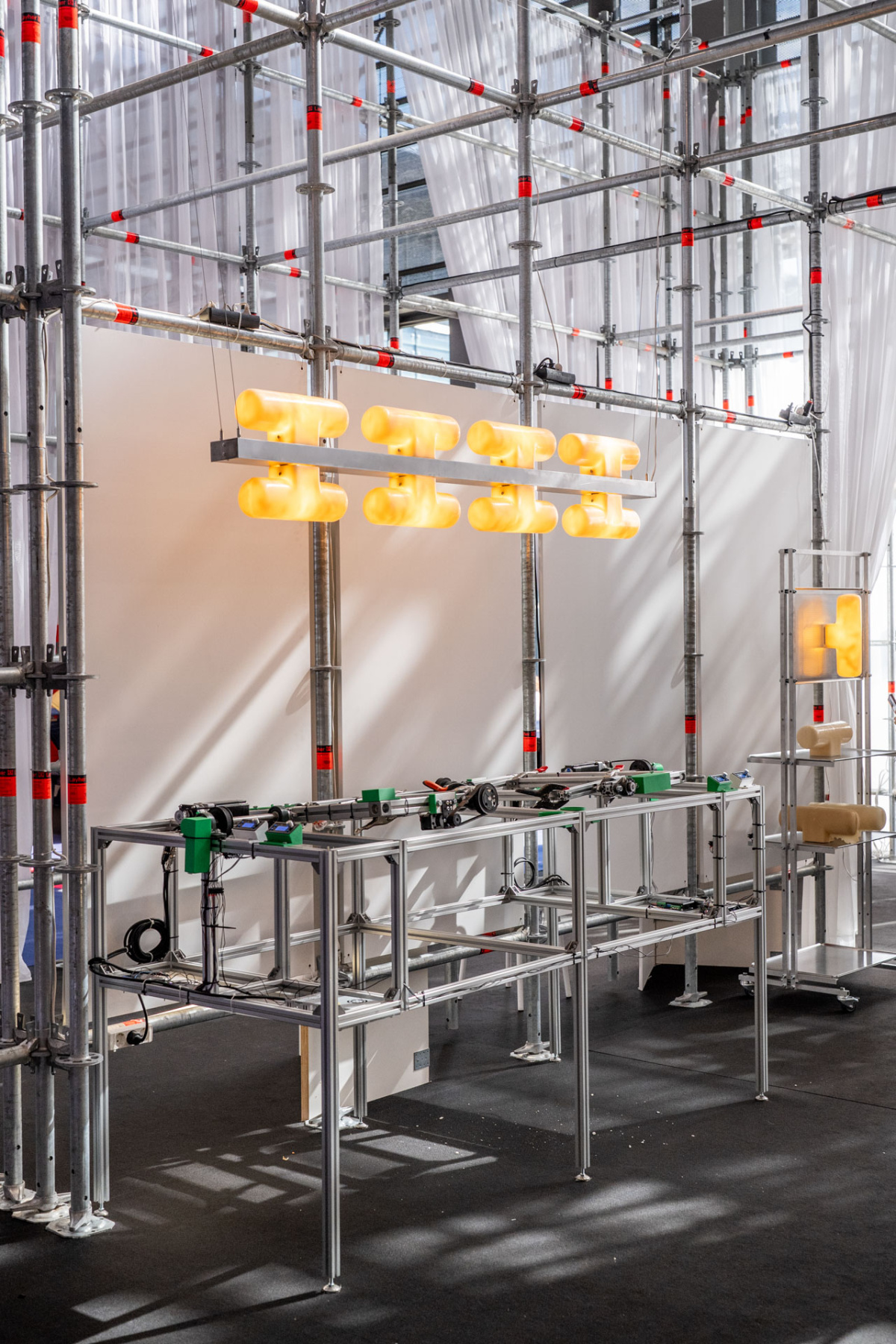 Yellow wax pendant lights hanging from a scaffold frame above a small machine