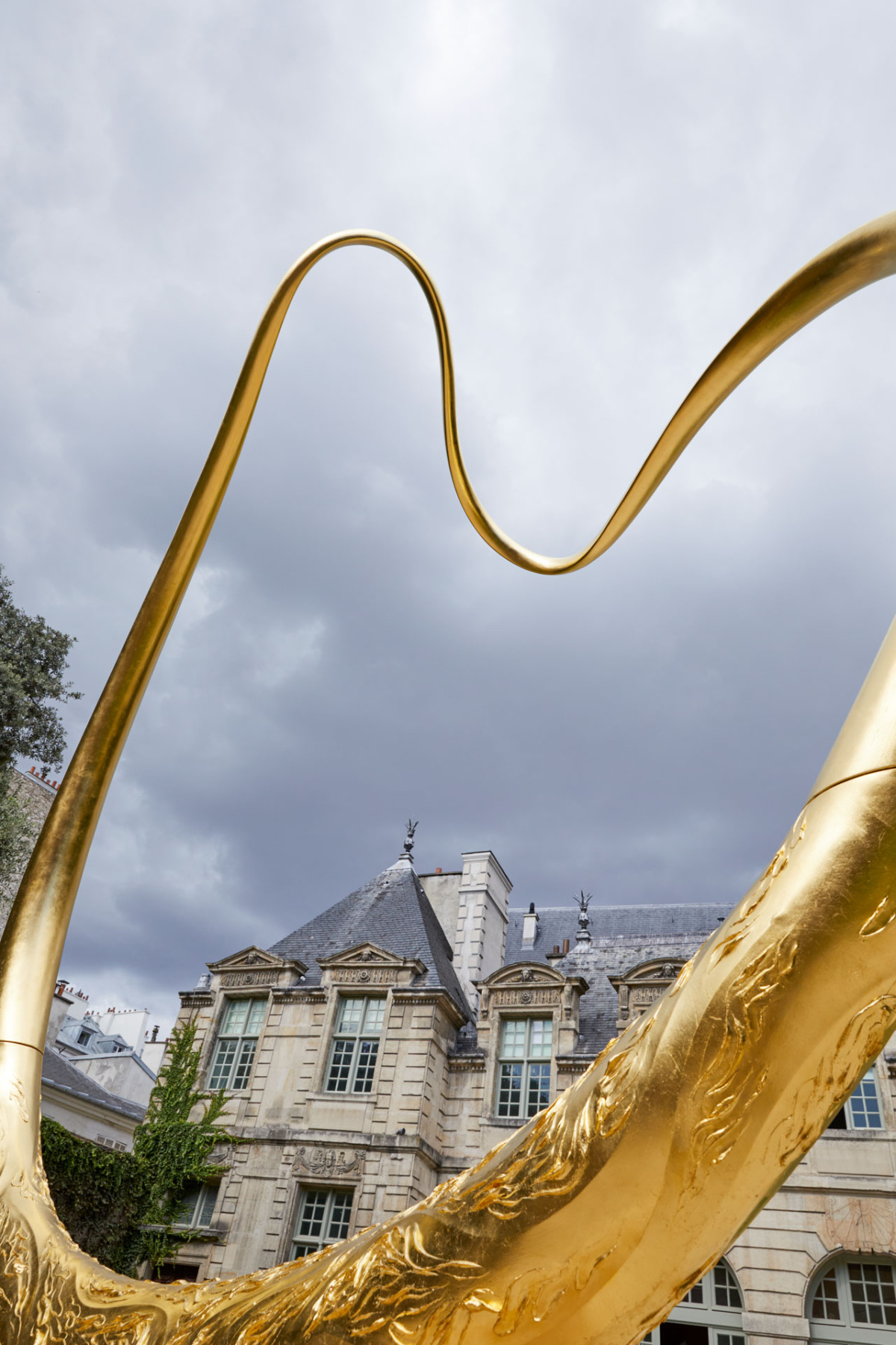 Gold curved sculpture rising over a Paris slate roof under grey sky