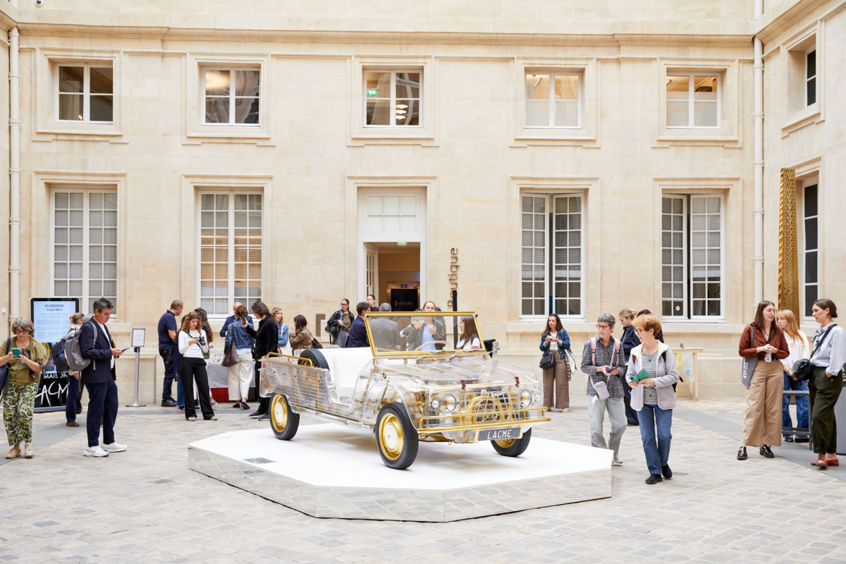 Transparent car with gold wheels on a mirrored plinth in a stone courtyard