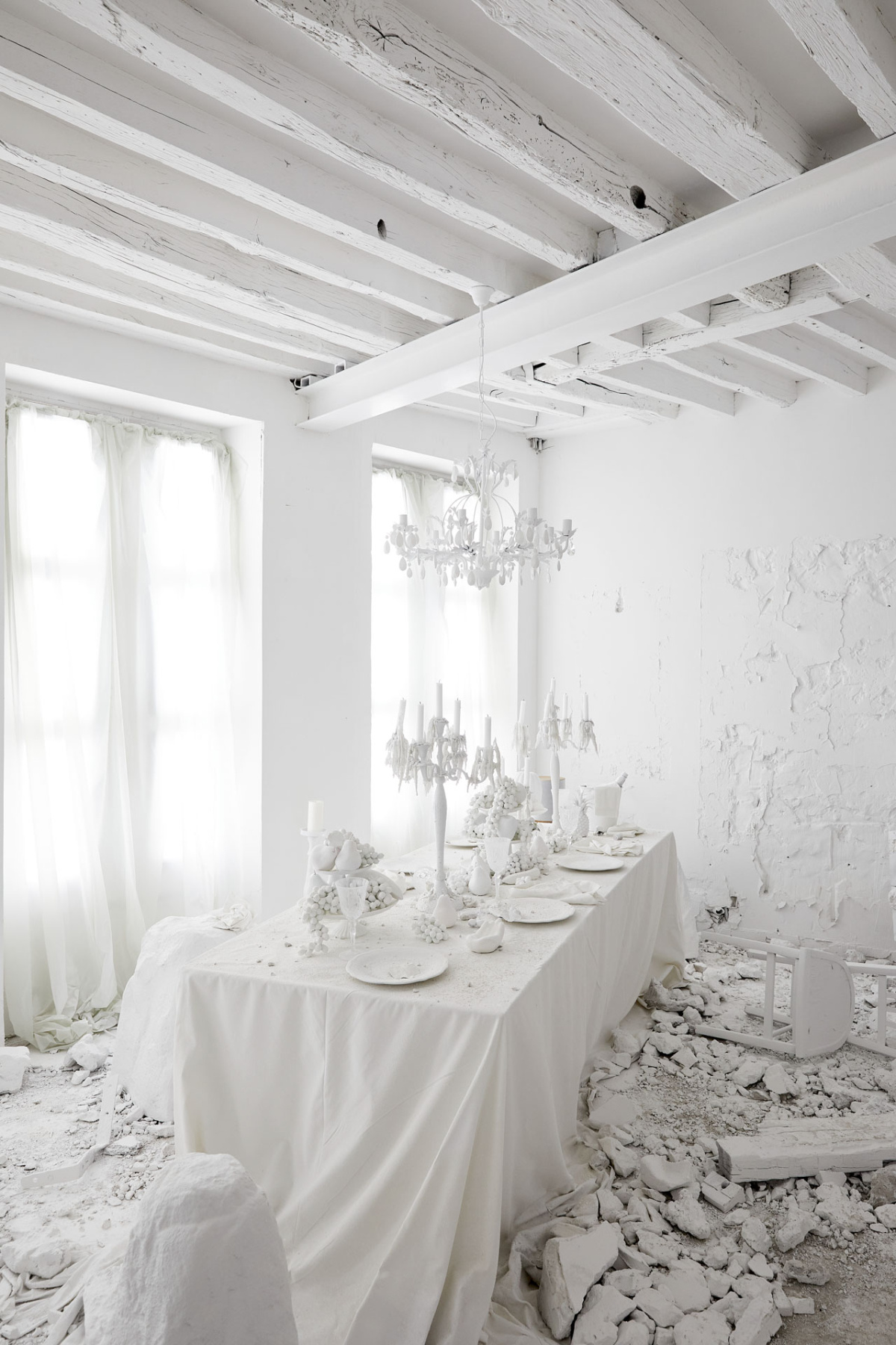 Dining room where the table, chandelier, and rubble are all coated in white plaster
