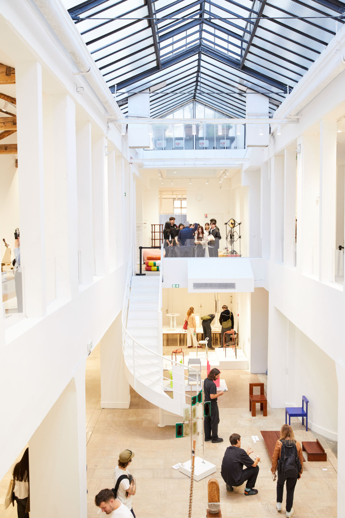White skylit atrium with a spiral staircase and visitors viewing small furniture