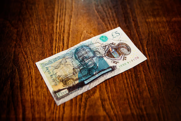 A British five-pound note lying on a dark wood table, printed side up.