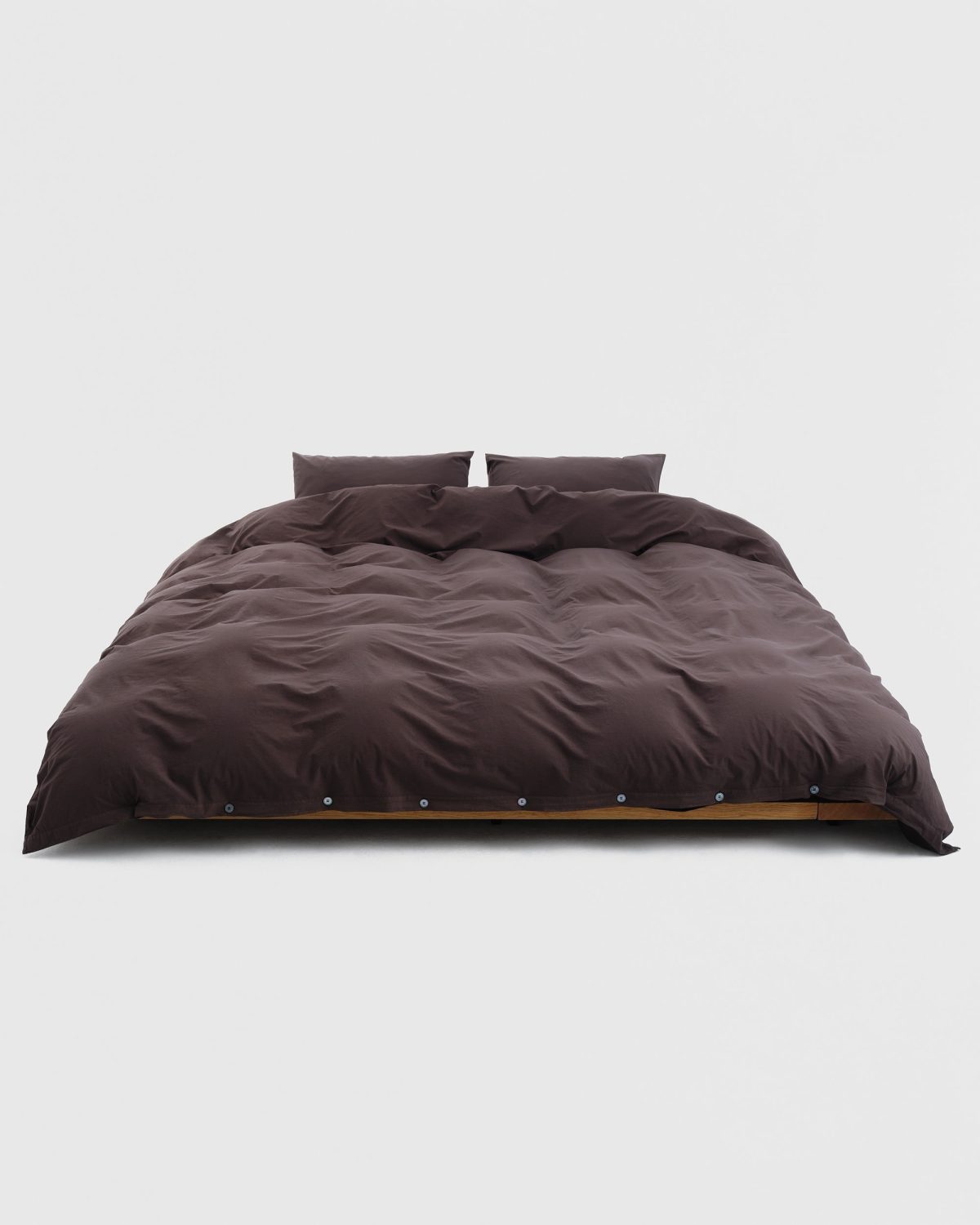 A bed made up with a deep brown percale duvet cover and pillowcases.