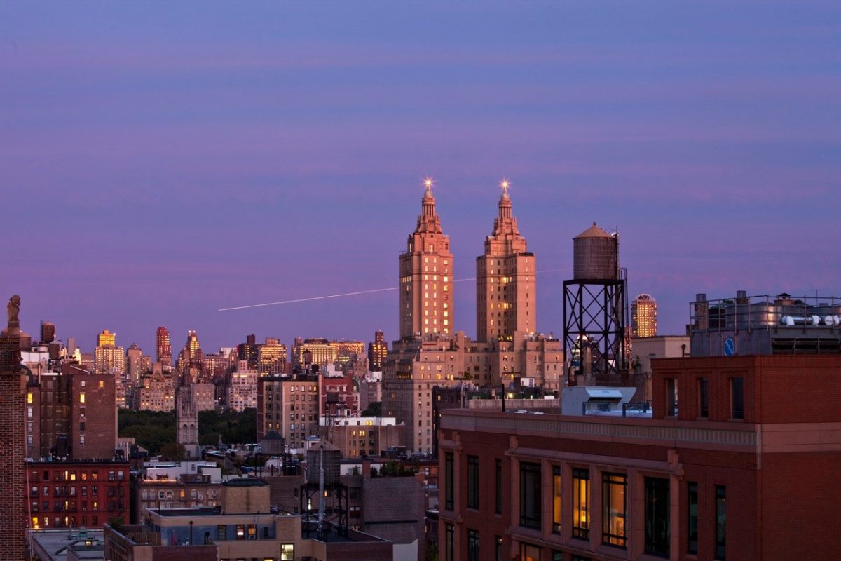 A dusk view over Upper West Side rooftops and water towers toward the twin towers of the San Remo.
